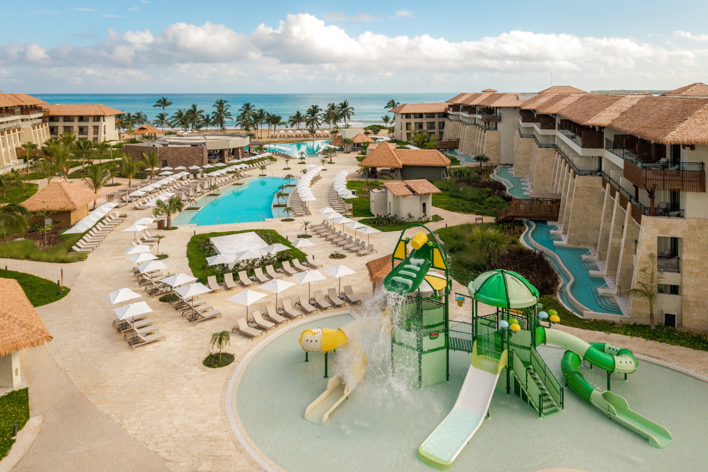 High-angle view of the kids' waterpark, long winding pool and resort buildings toward the sea.