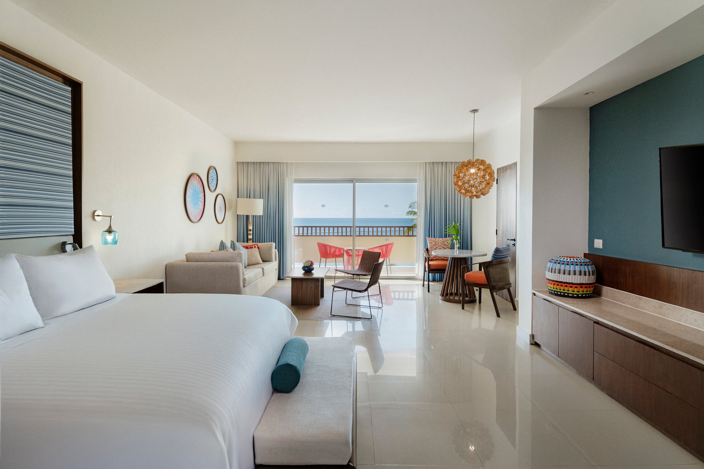 Master oceanfront suite with a king bed, living area, round dining table, woven pendant lights and sliding doors to an ocean balcony.