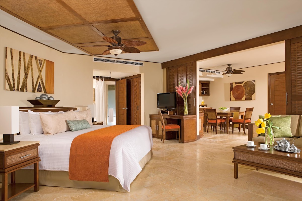 Spacious suite with king bed, living area, dining table, and wooden furnishings throughout at Dreams Riviera Cancun Resort & Spa.