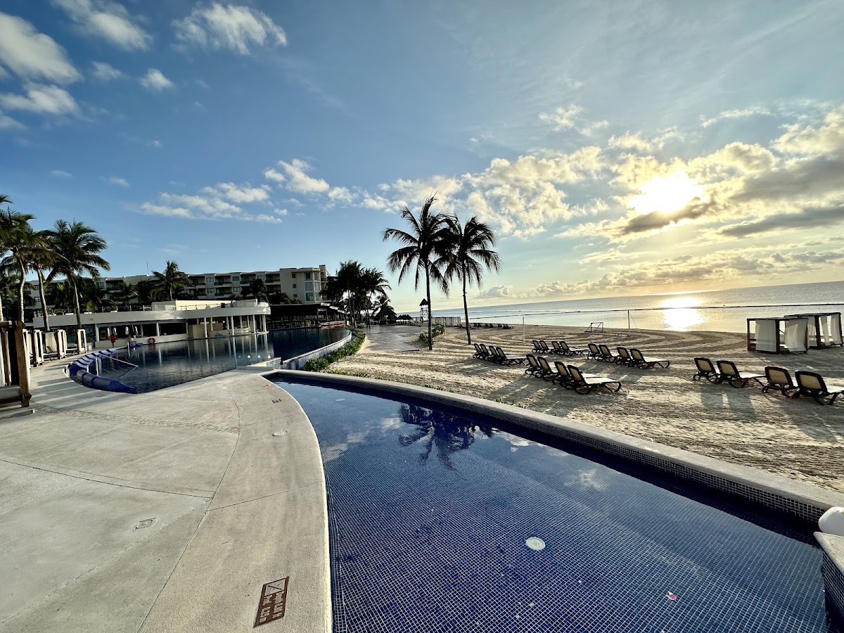 Resort pools and beachfront with lounge chairs, palm trees, and ocean view at sunrise or sunset.