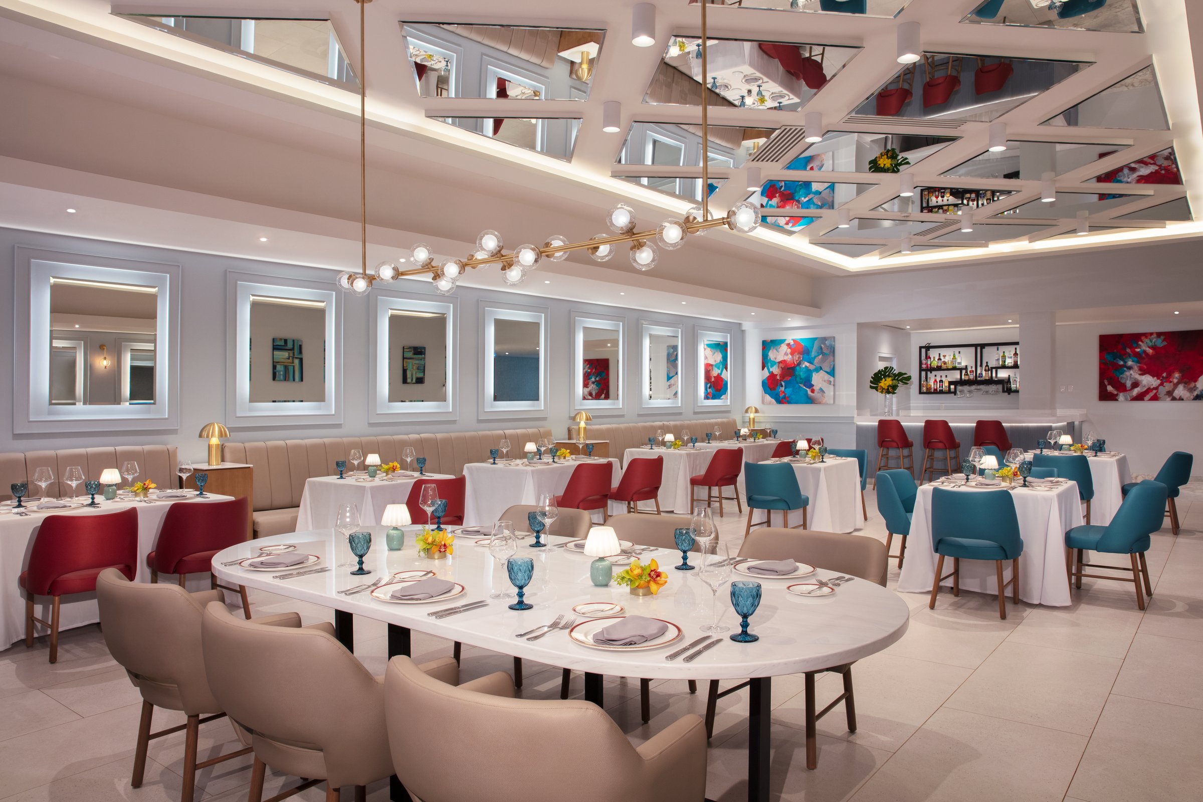 Portofino restaurant with a coffered mirrored ceiling, a gold branch chandelier, white-clothed tables and a large oval communal table.