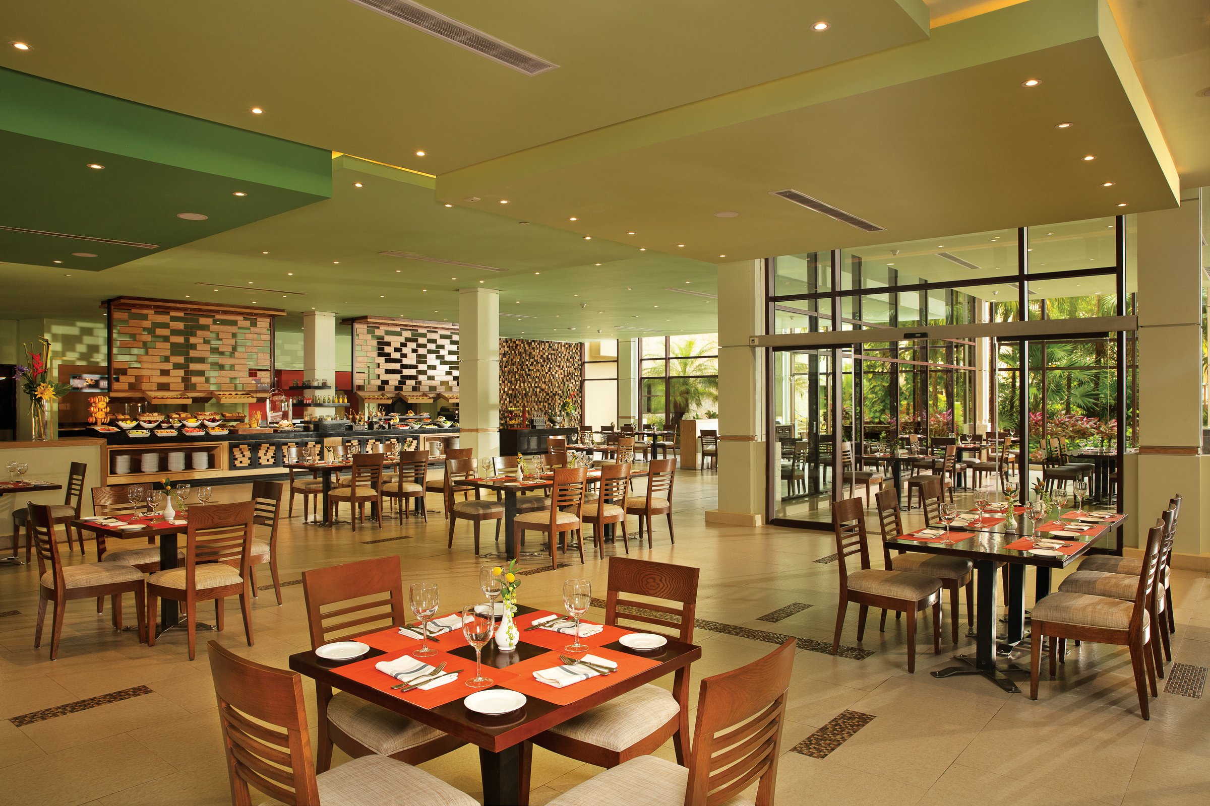 World Cafe buffet restaurant with rows of wooden tables, red placemats and floor-to-ceiling windows onto tropical plants.