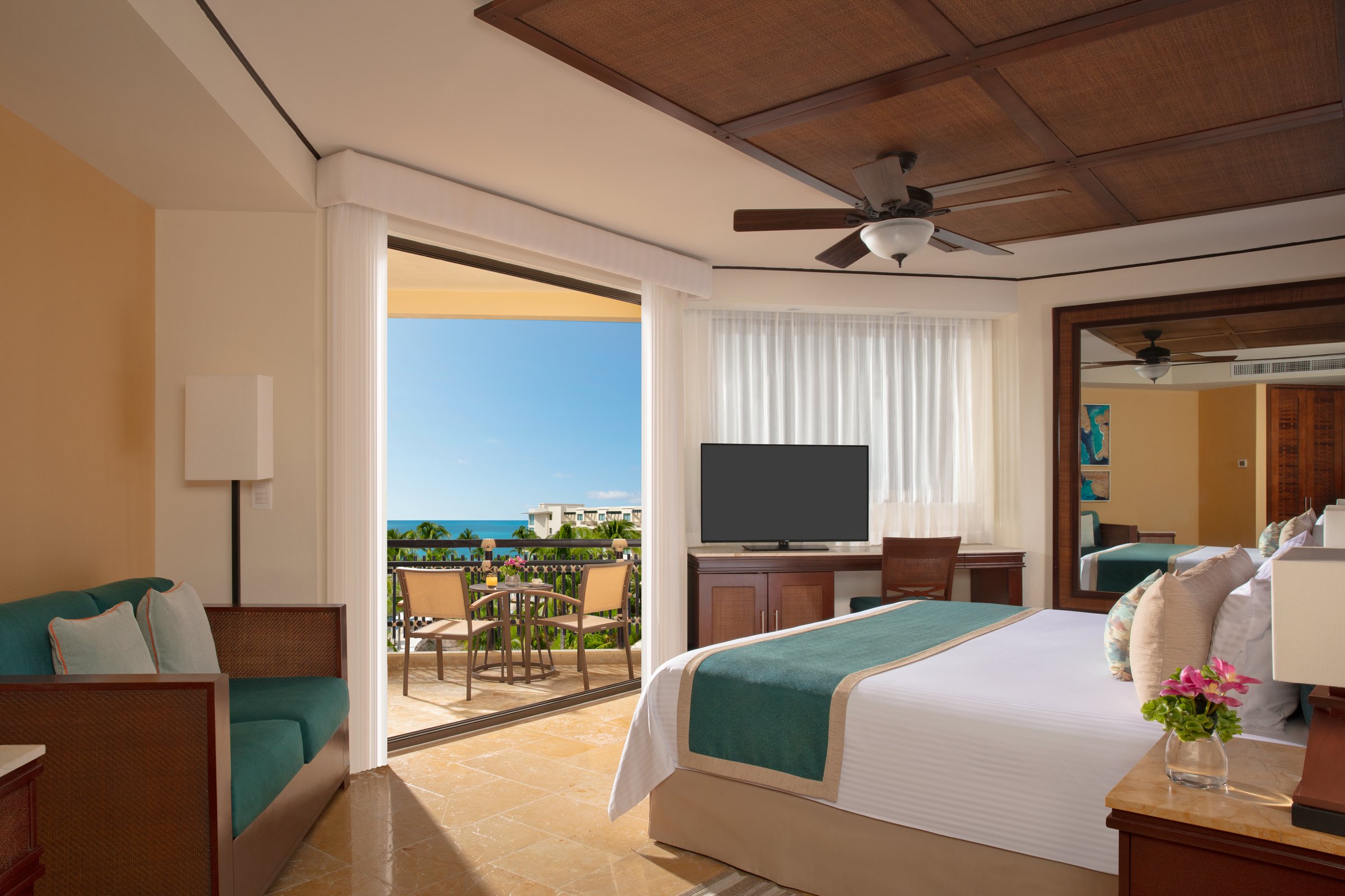 Deluxe ocean view room with a king bed, green sofa and an open balcony door looking to the sea.