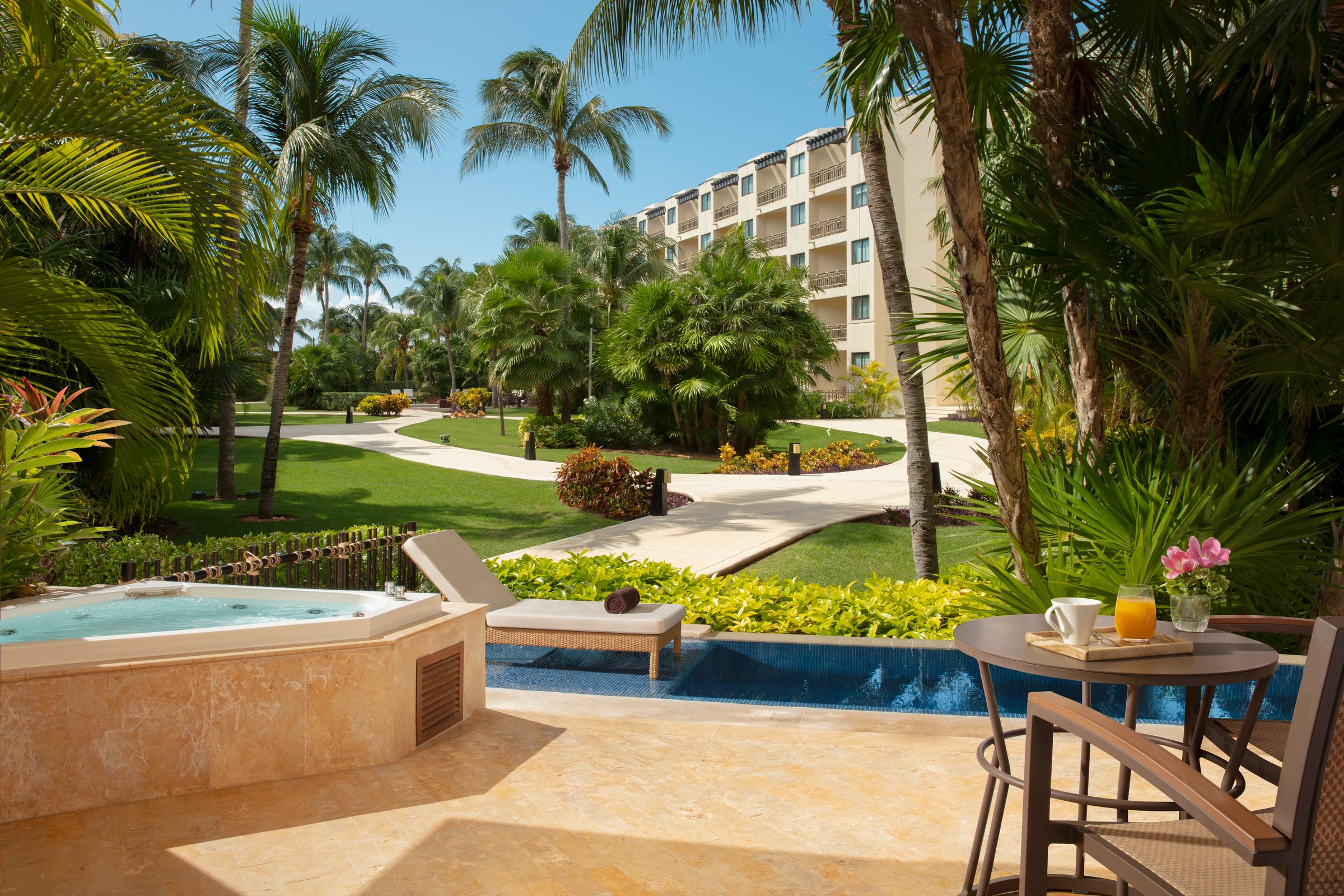 Ground-floor terrace with a whirlpool tub, breakfast table and a private plunge pool, with lawns and palms beyond.