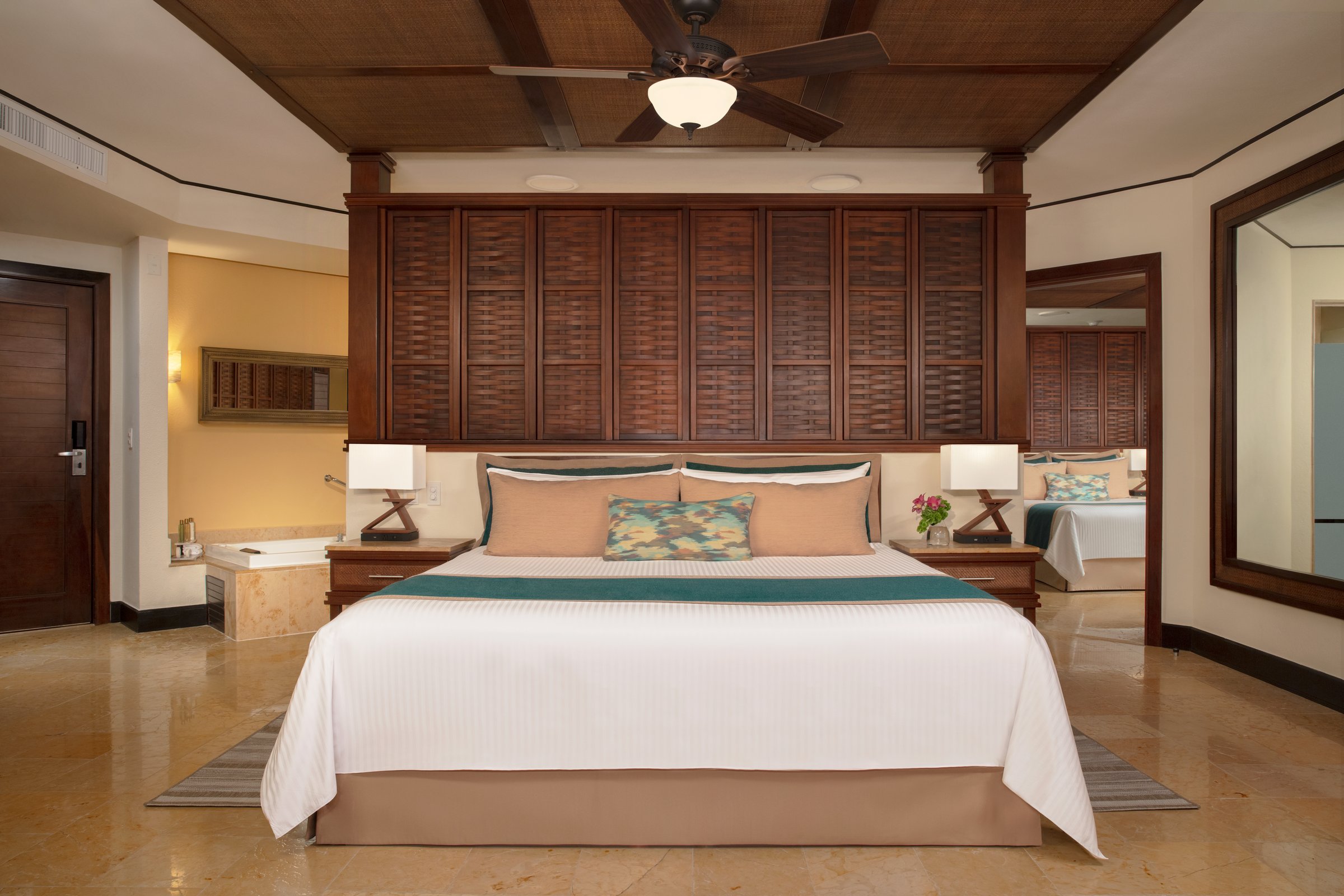 Family suite bedroom with a king bed, a dark wood louvered headboard wall and a corner jetted tub, with a second bedroom beyond.