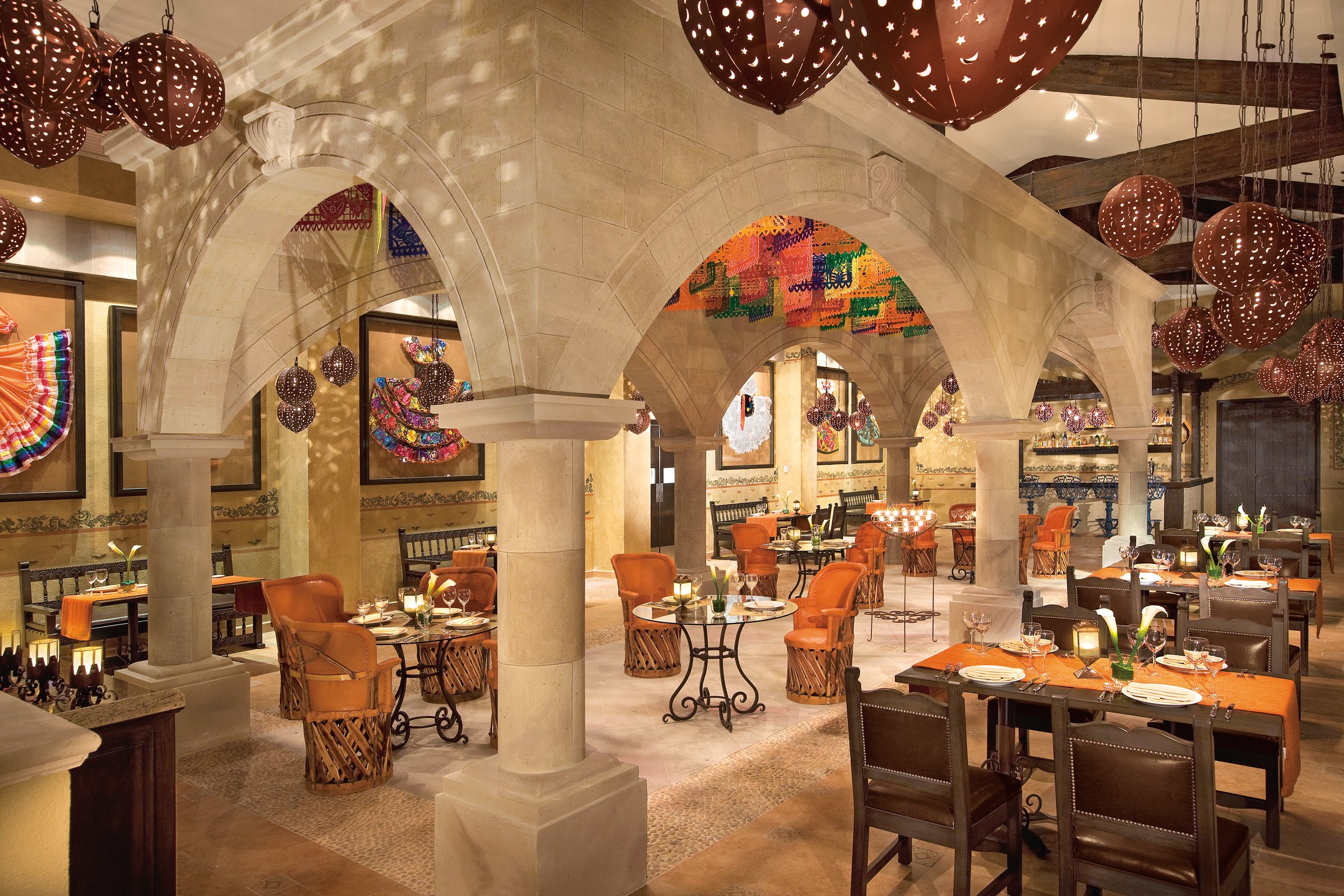 El Patio restaurant under stone arches and dark beams, with round red lanterns hanging over rustic wood and leather chairs.