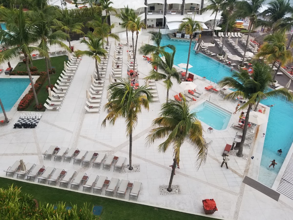 Aerial view of Dreams Vallarta Bay Resort & Spa with multiple pools, lounge chairs, palm trees, and white buildings surrounding the pool deck.