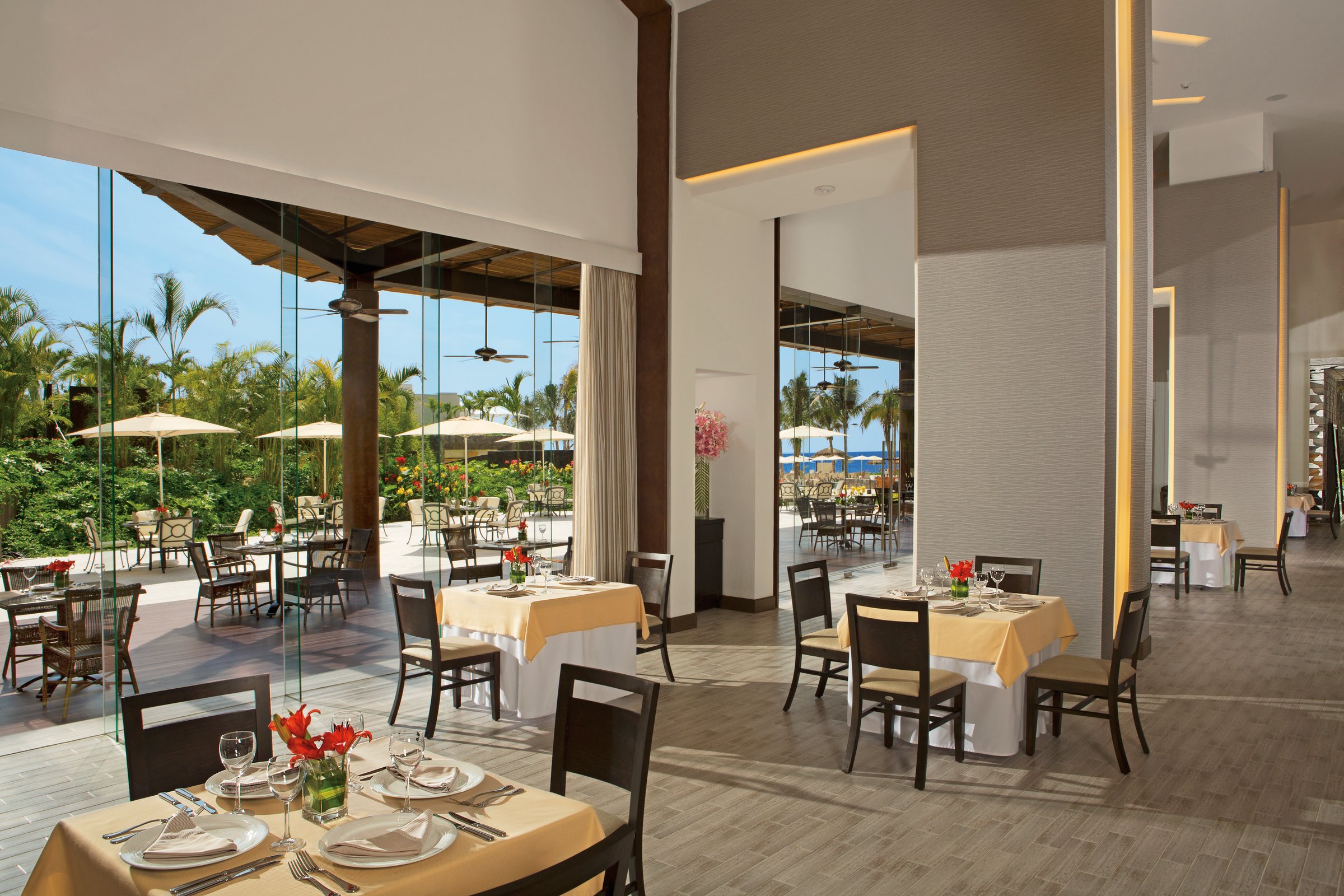 Carnival restaurant with set tables and open glass doors to a shaded terrace.
