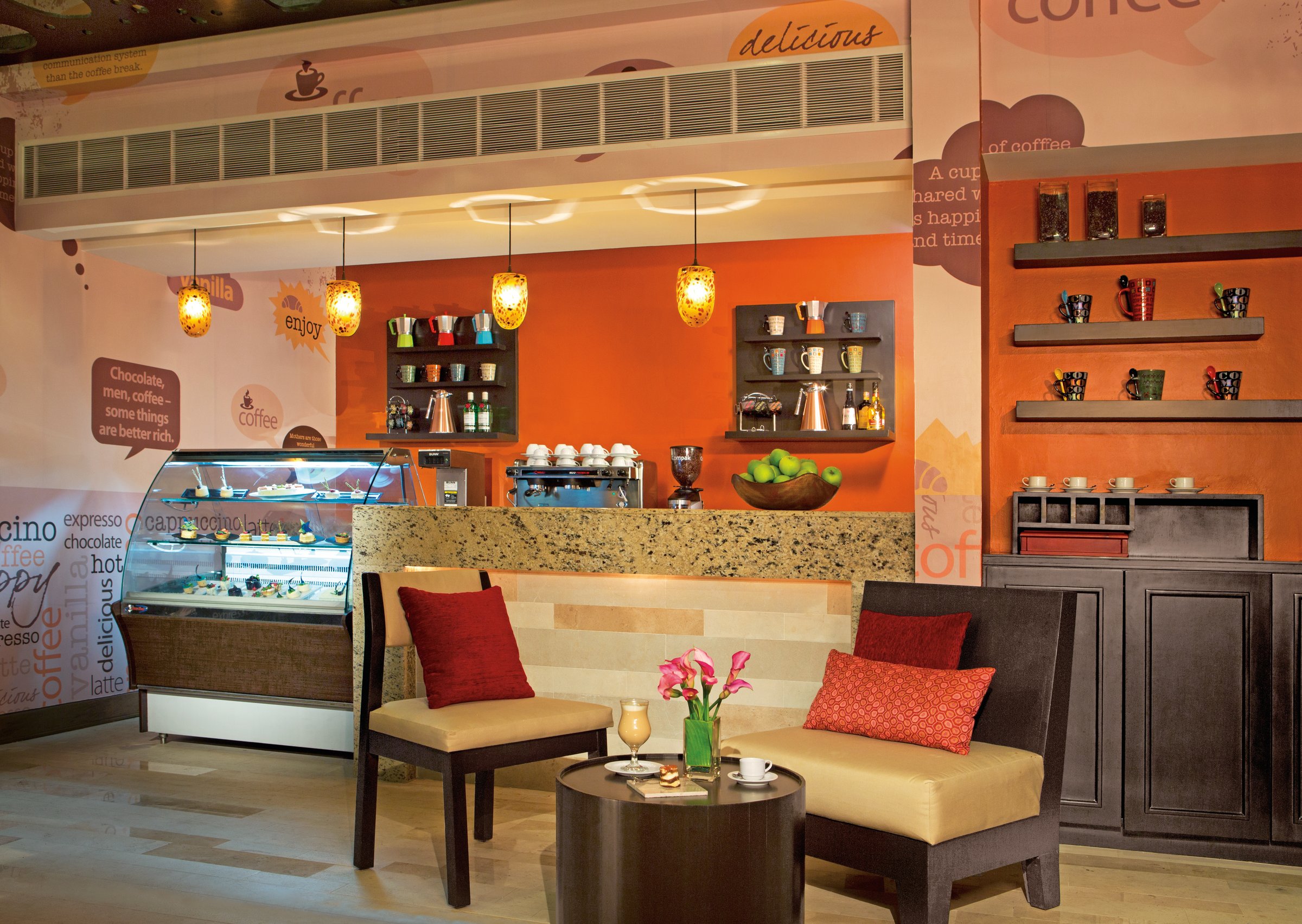 Coco Cafe counter with pastry case, orange wall and pendant lights.