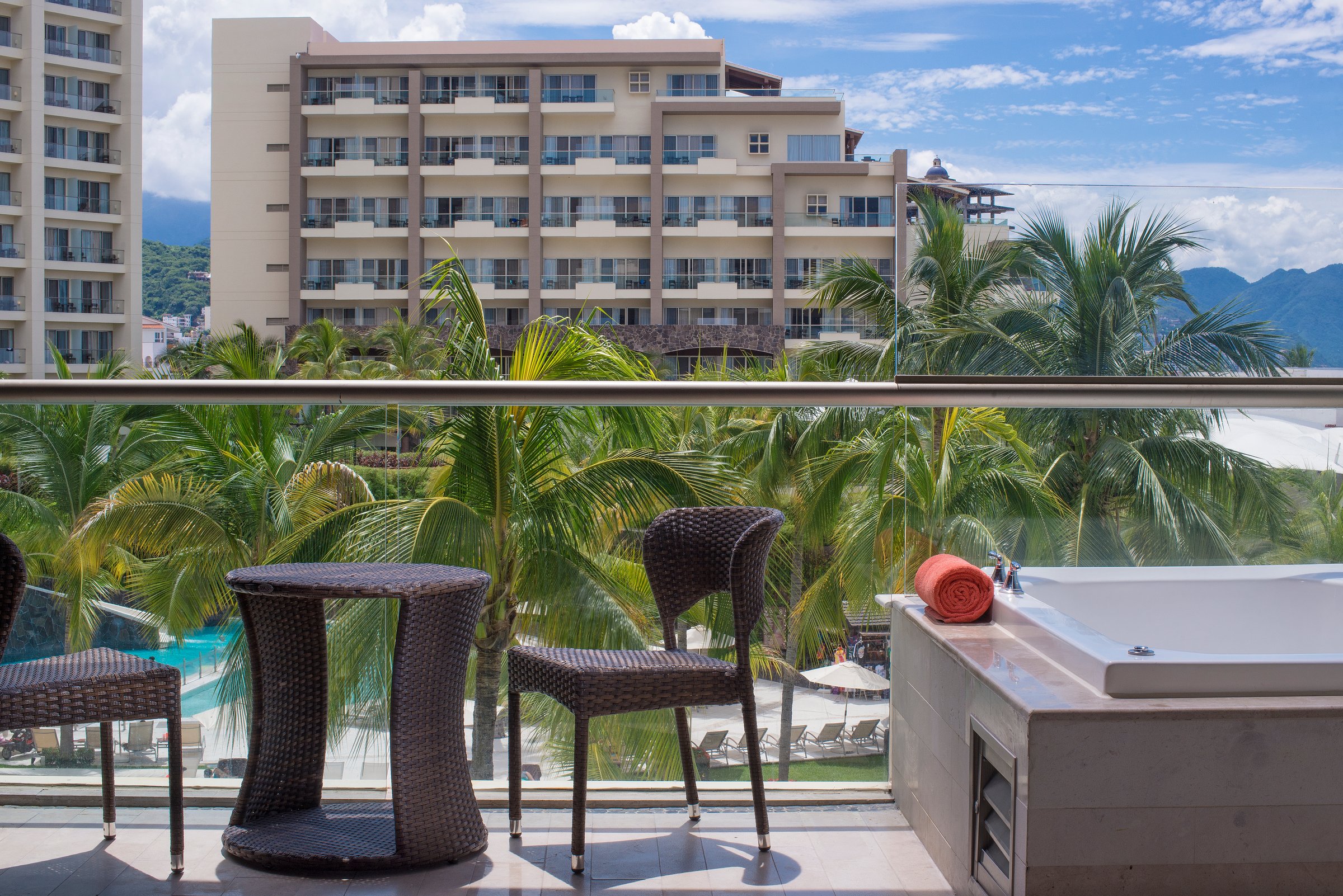 Junior suite garden-view balcony with wicker chairs, soaking tub and palms.