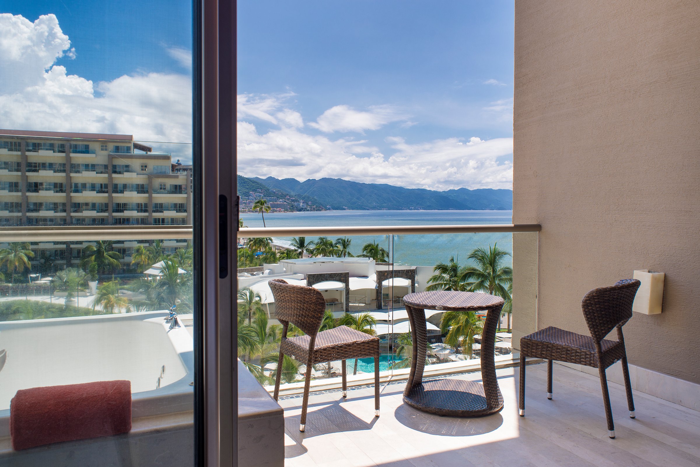 Junior suite ocean-view balcony with wicker seating, soaking tub and a view of the bay.