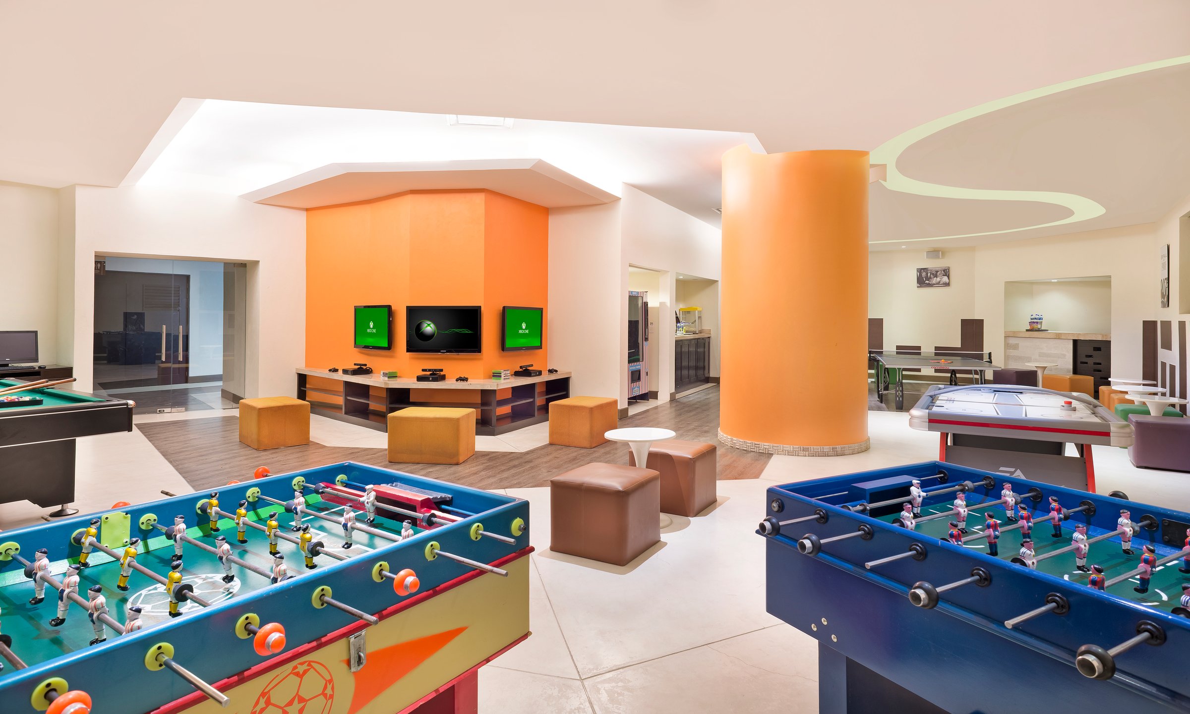 Core Zone game room with foosball, pool and air hockey tables and TVs on an orange wall.