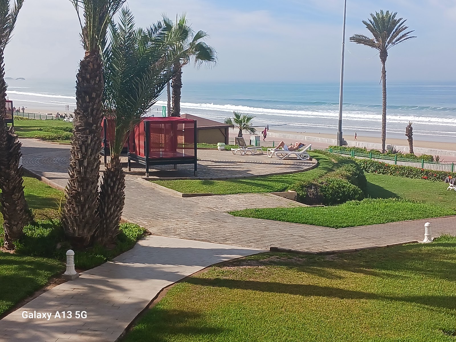 Palm-lined grounds with paved pathways, a red structure, and lounge chairs facing the beach and ocean at Dunes d'Or Ocean Club.