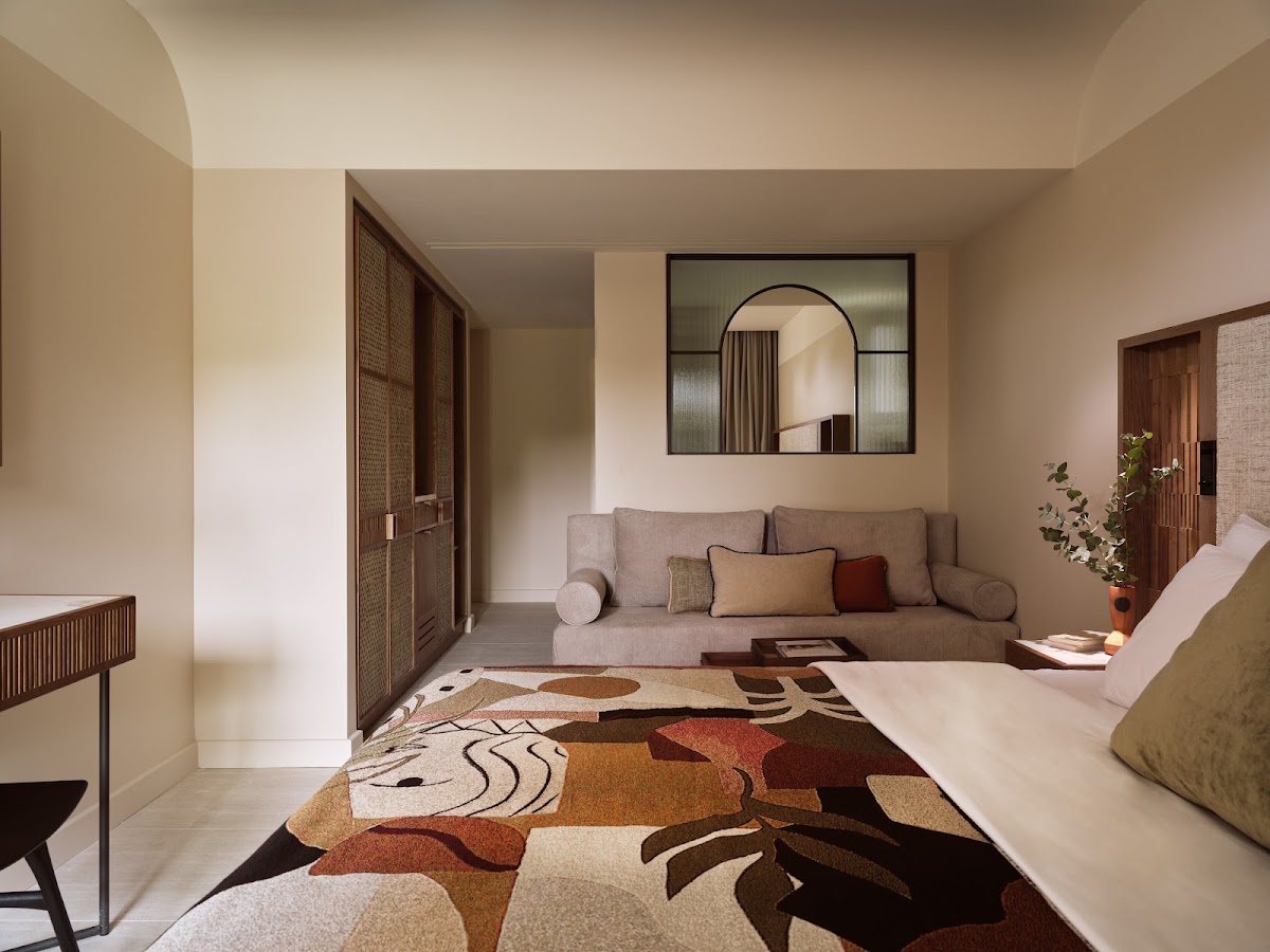 Spacious resort suite with beige walls, gray sofa, patterned area rug, and a framed mirror above seating area.