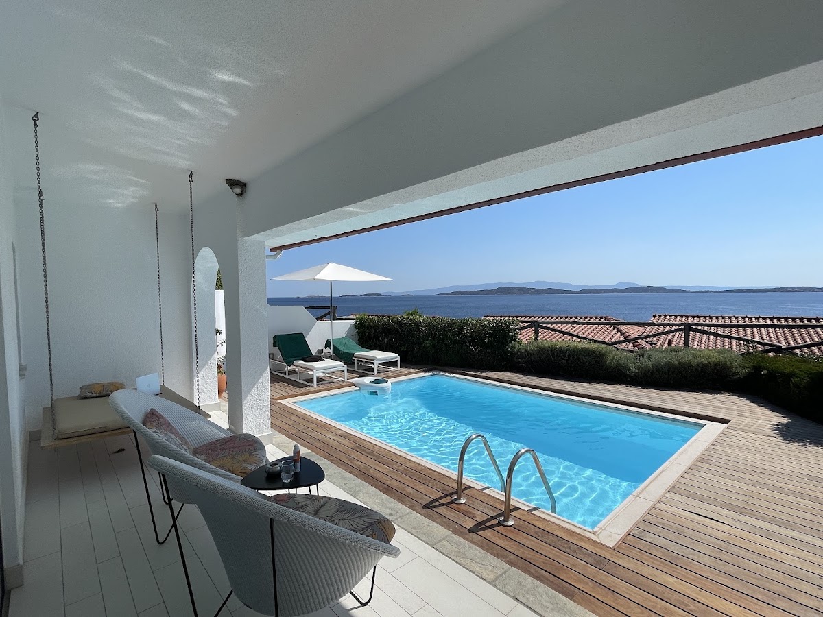 Private pool terrace at Eagles Palace overlooks the Aegean Sea with lounge chairs, white umbrella, and clear blue water.