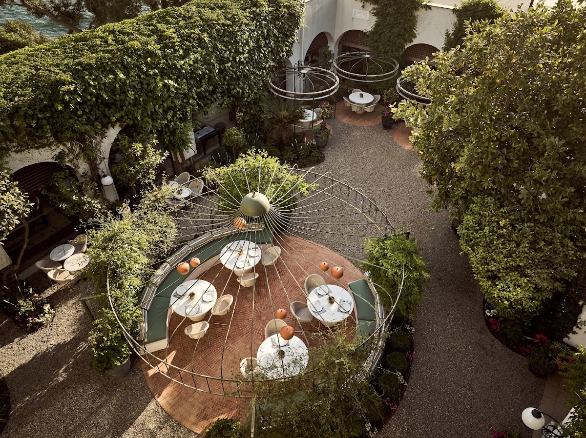 Overhead view of a courtyard dining area surrounded by ivy-covered walls, with round tables under parasols and a central circular table set for a meal.