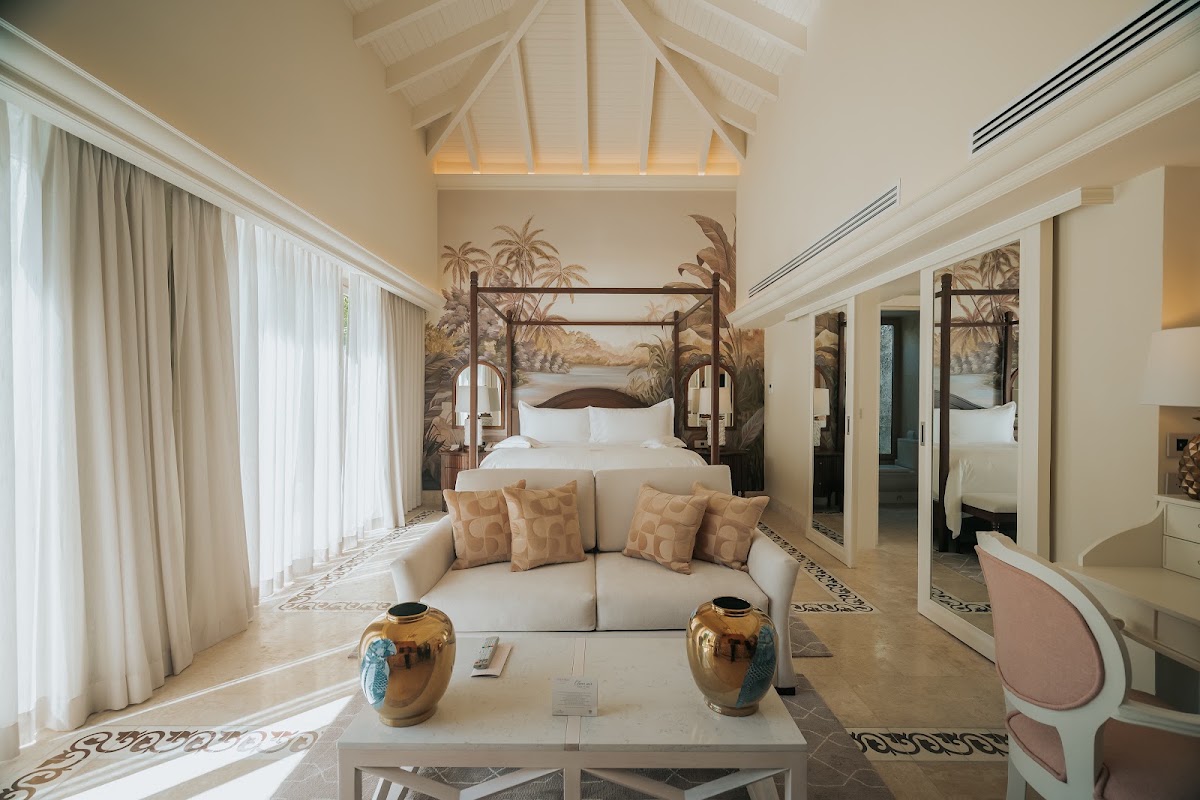 Spacious resort suite with four-poster bed, cream sofa with patterned pillows, and decorative brass vases at Eden Roc Cap Cana.