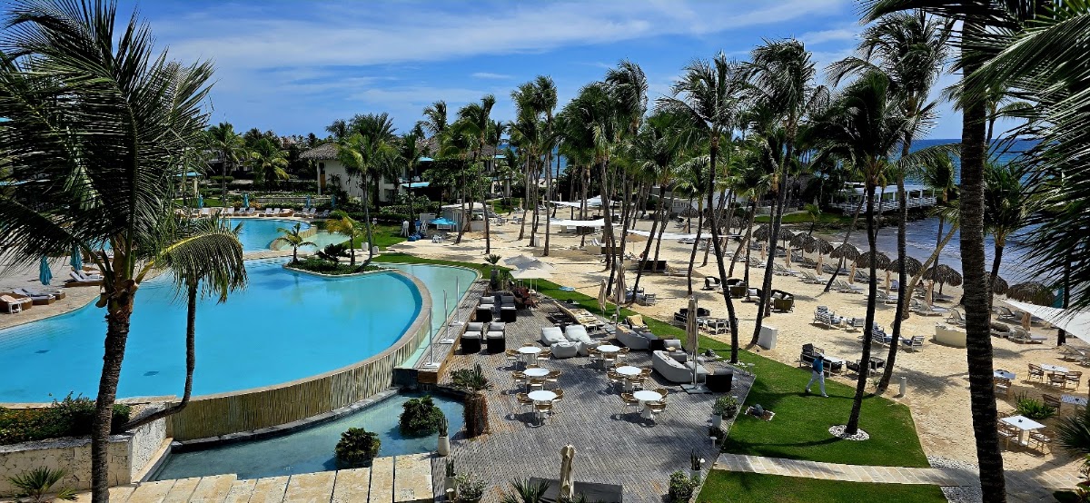 Curved pool with lounge chairs and palm trees overlooking a sandy beach and ocean at Eden Roc Cap Cana.