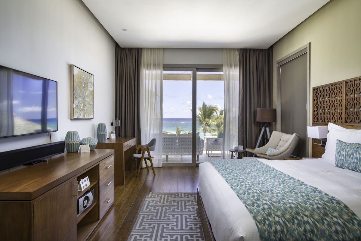 Spacious beachfront room at Eden Roc Cap Cana with king bed, ocean view balcony, and modern furnishings overlooking palm trees and turquoise water.