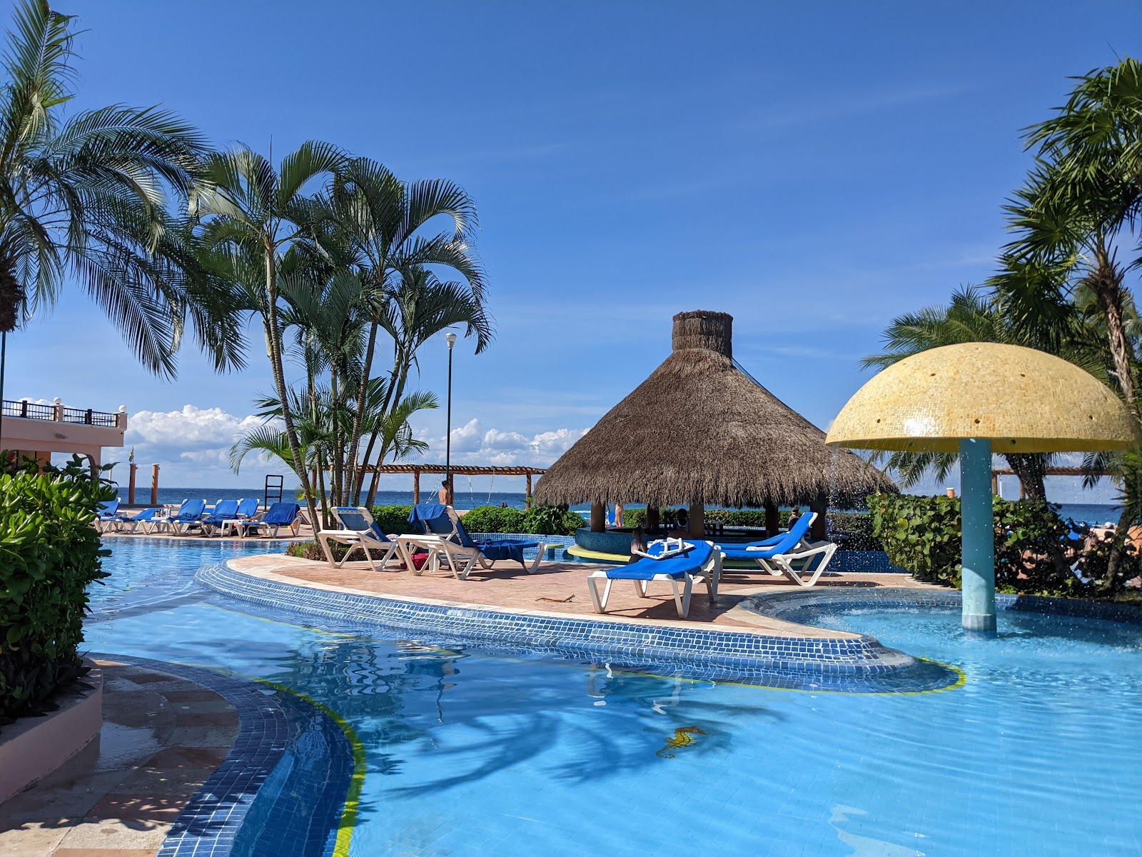 Indoor pool area at dusk with curved design, lounge chairs, lit columns, and mountain views through archways at El Cozumeleño Beach Resort.