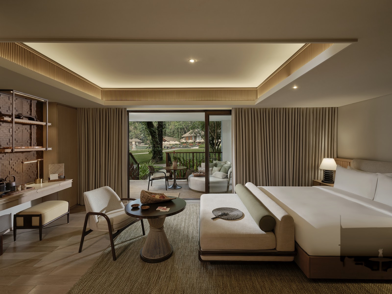 Resort suite with cream bed, lounge seating, and sliding glass doors opening to a private deck overlooking manicured grounds and distant bungalows.