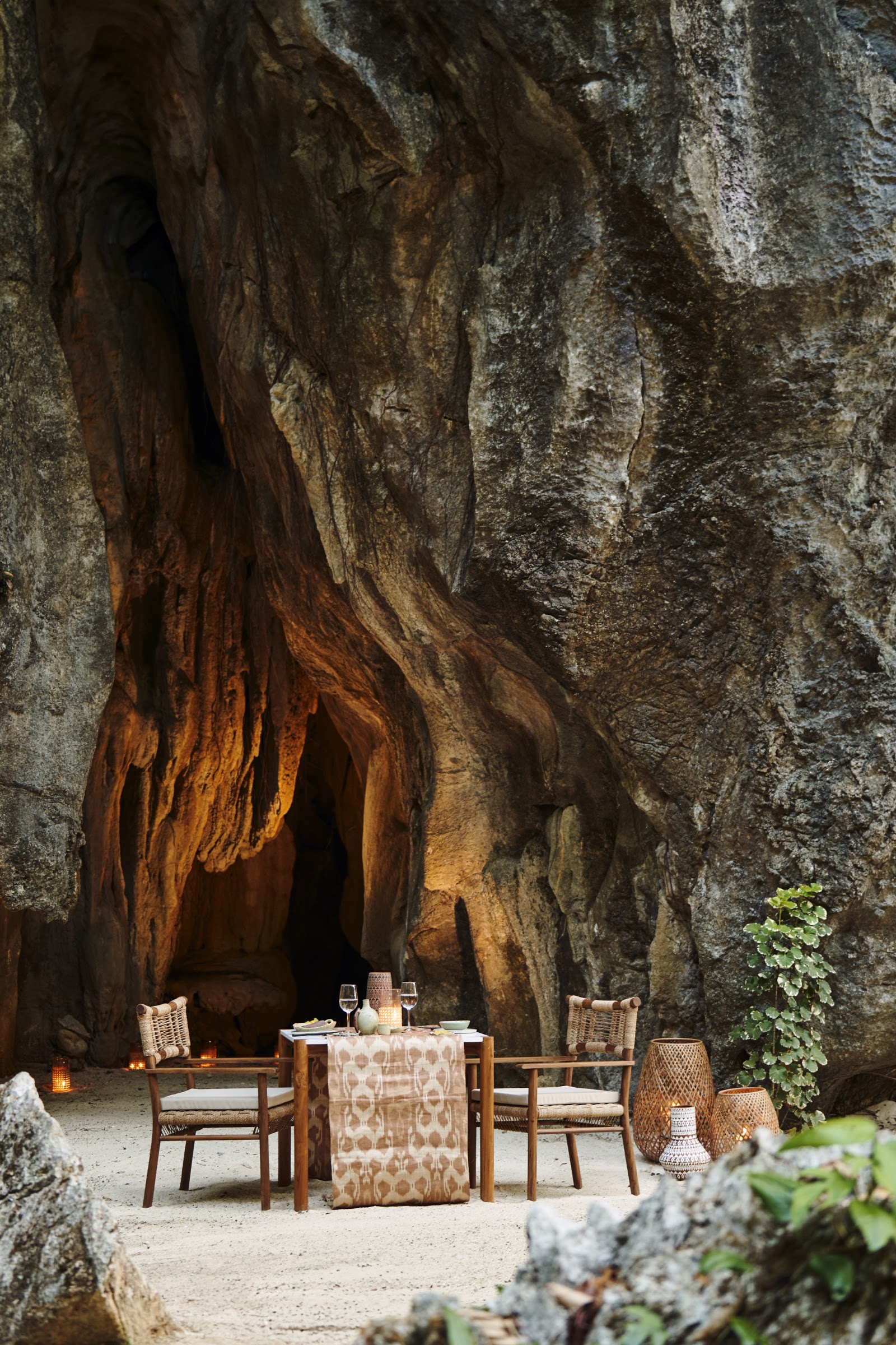 Intimate dining setup nestled in a cave with towering rock walls, two wicker chairs, and a table set for two at El Nido Resorts Lagen Island.