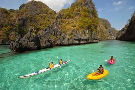 Guests kayaking and floating on inflatable rings in turquoise water surrounded by dramatic limestone cliffs at El Nido Resorts Miniloc Island.