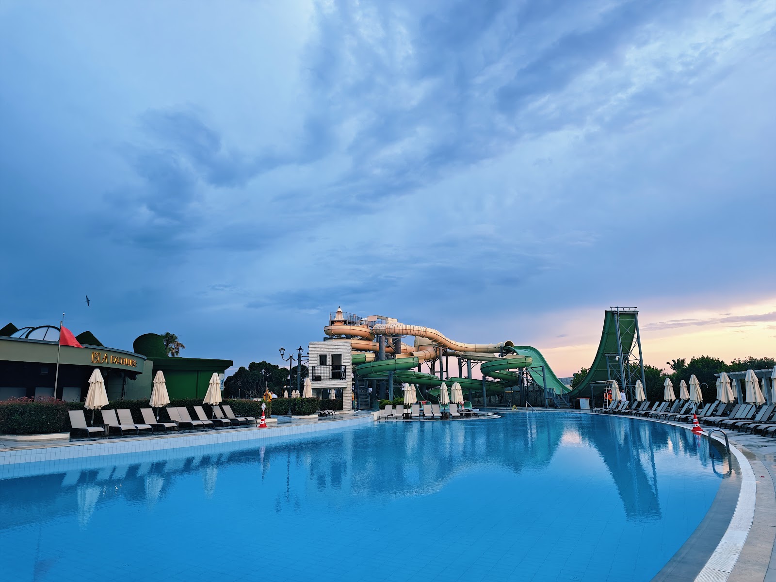 Large pool with water slides and loungers at dusk, Ela Excellence Resort Belek in Turkey.