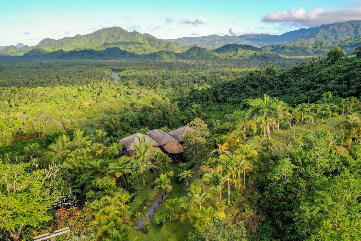 Emaho Sekawa Retreat Fiji nestled in lush valley vegetation with thatched-roof buildings, a river, and forested mountains in the background.