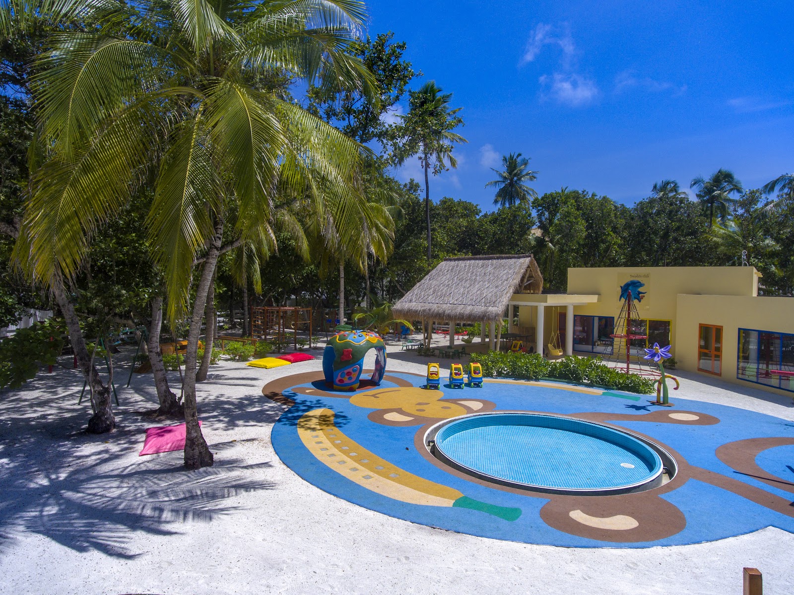 Kids' water play area with colorful blue ground design, inflatable toys, and shallow pool surrounded by palm trees at Emerald Maldives Resort & Spa.