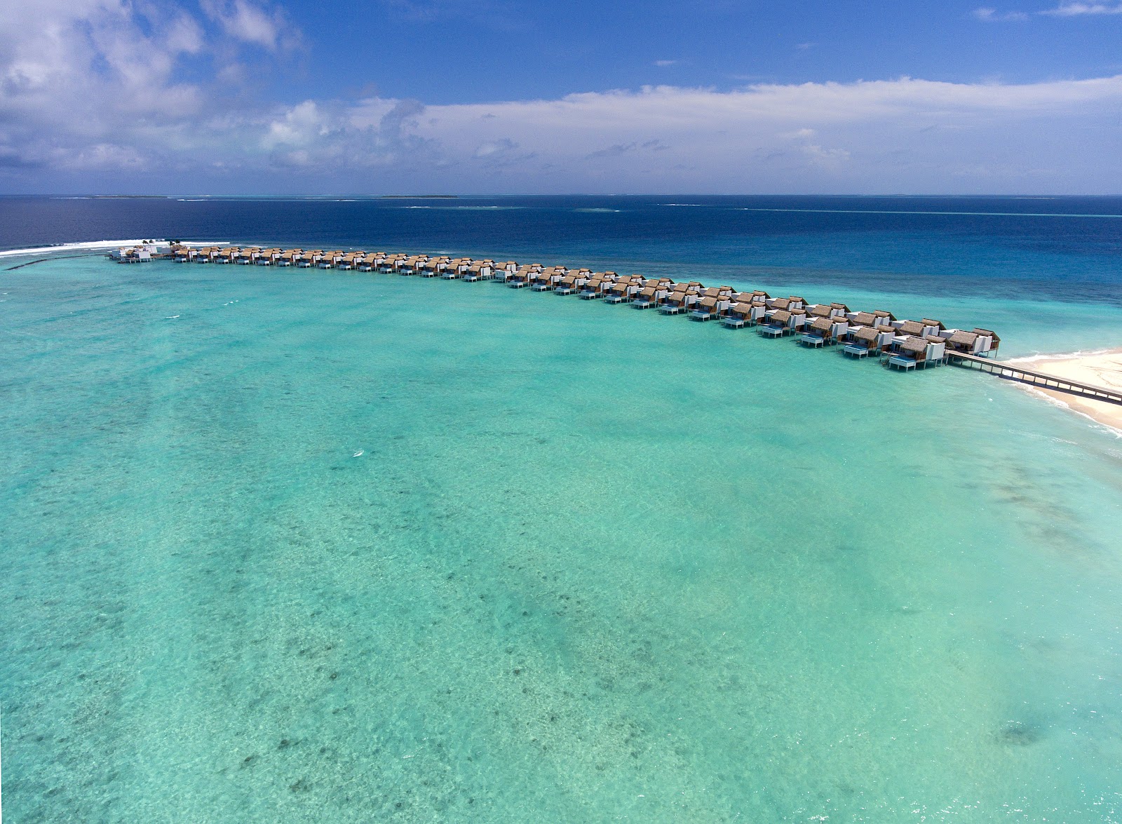 Rows of thatched overwater bungalows line a wooden jetty extending into turquoise lagoon waters at Emerald Maldives Resort & Spa.