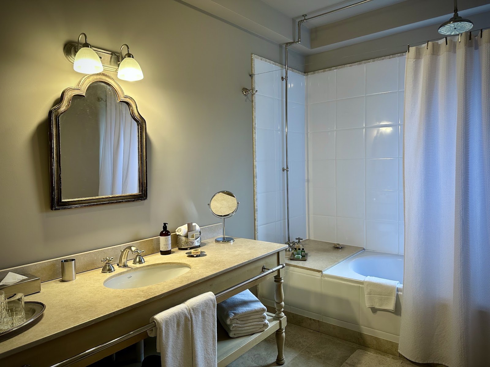 Resort bathroom with marble vanity, arched mirror with sconces, soaking tub, glass shower enclosure, and folded towels on shelf.