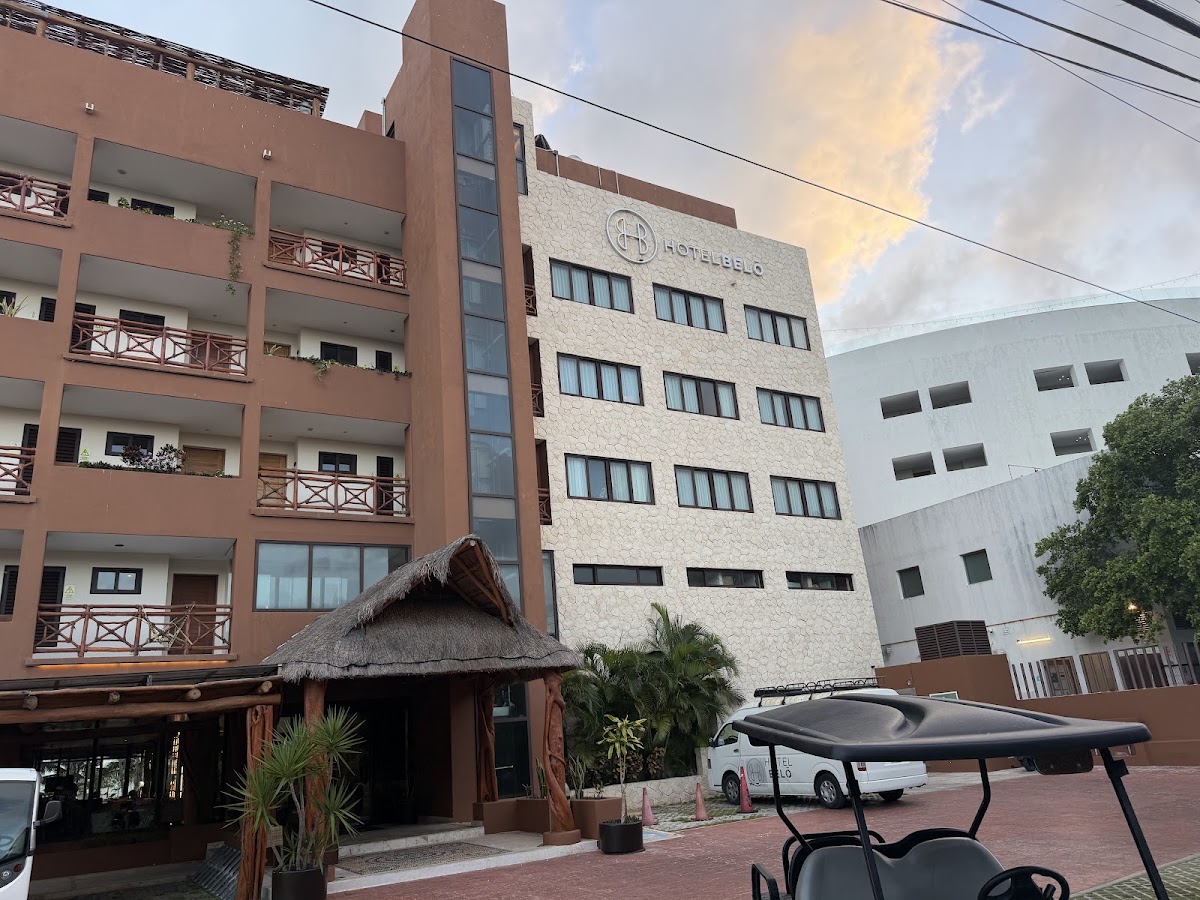 Hotel Esplendor exterior with multi-story tan and terracotta buildings, thatched-roof entrance, and golf cart in brick courtyard.