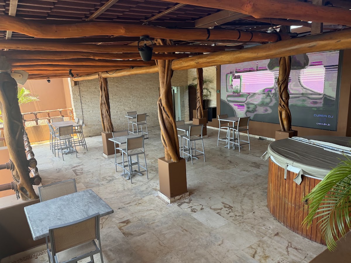 Covered outdoor bar and lounge area with wooden beams, high-top tables, and a large screen display at Esplendor by Wyndham Isla Mujeres.