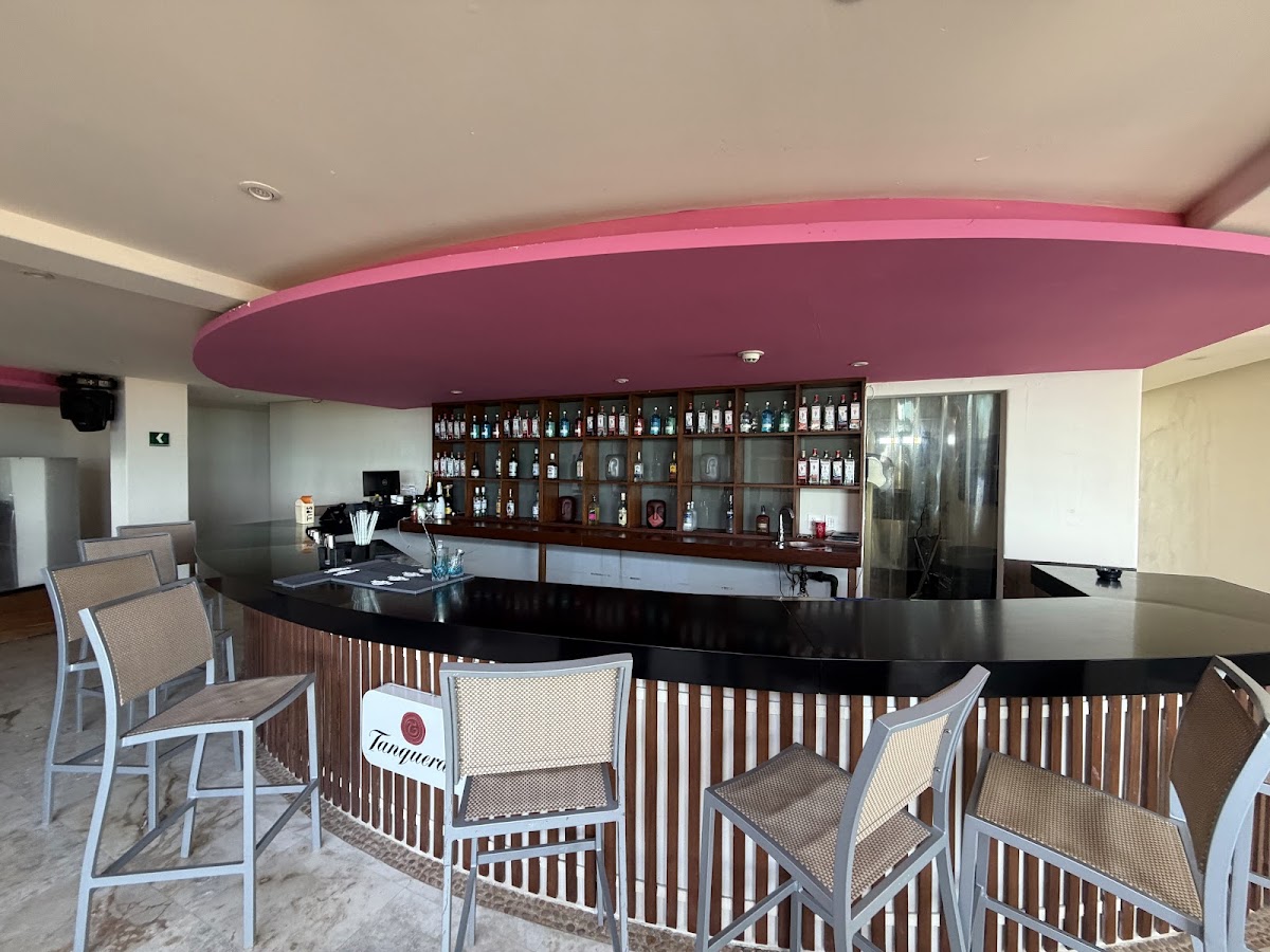 Bar seating area with curved pink ceiling, black counter, wood-slat railings, and stocked liquor shelves behind the counter.