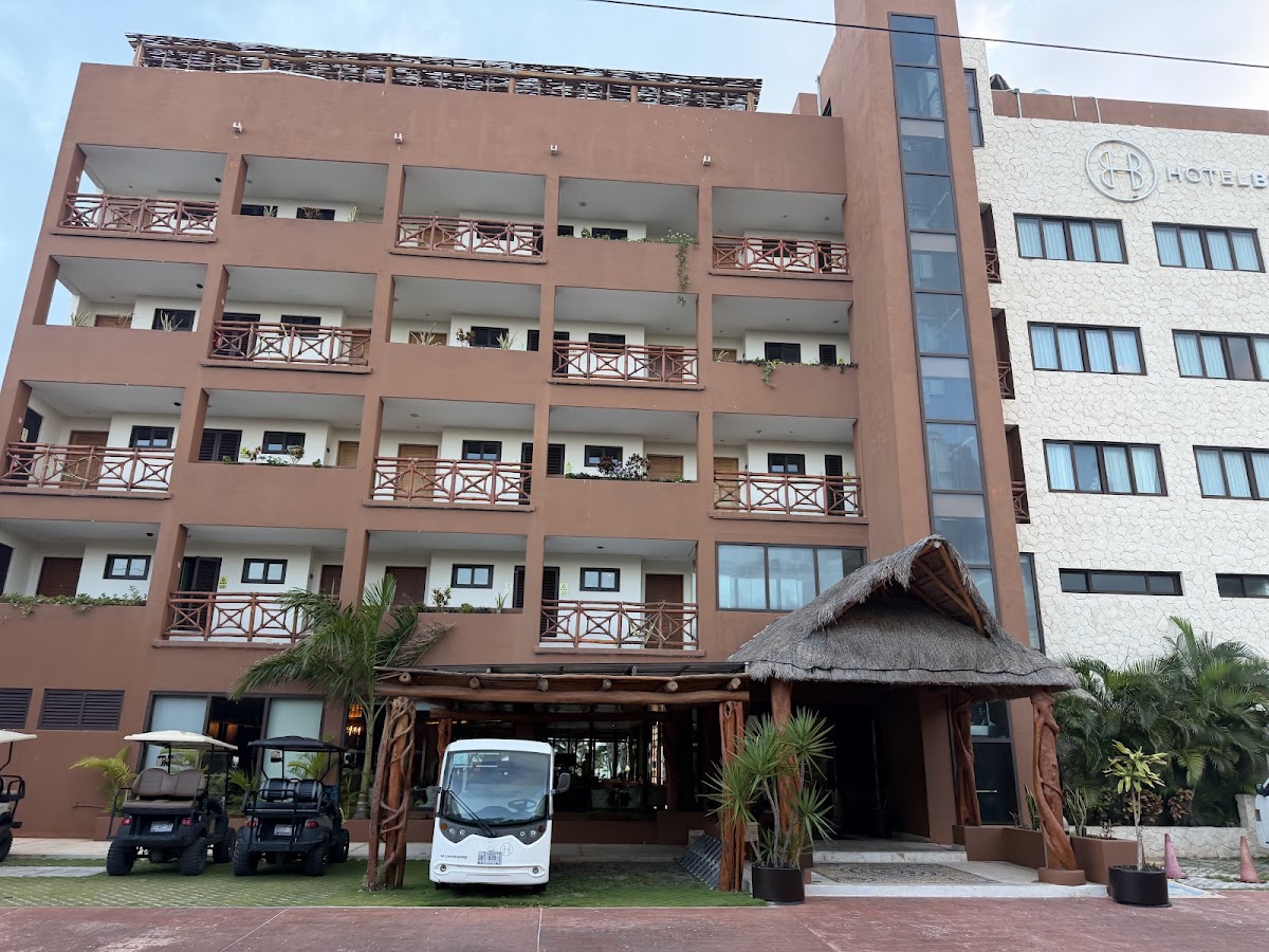 Terracotta resort building with multiple balconies, thatched-roof entrance, golf carts, and palm trees at ground level.