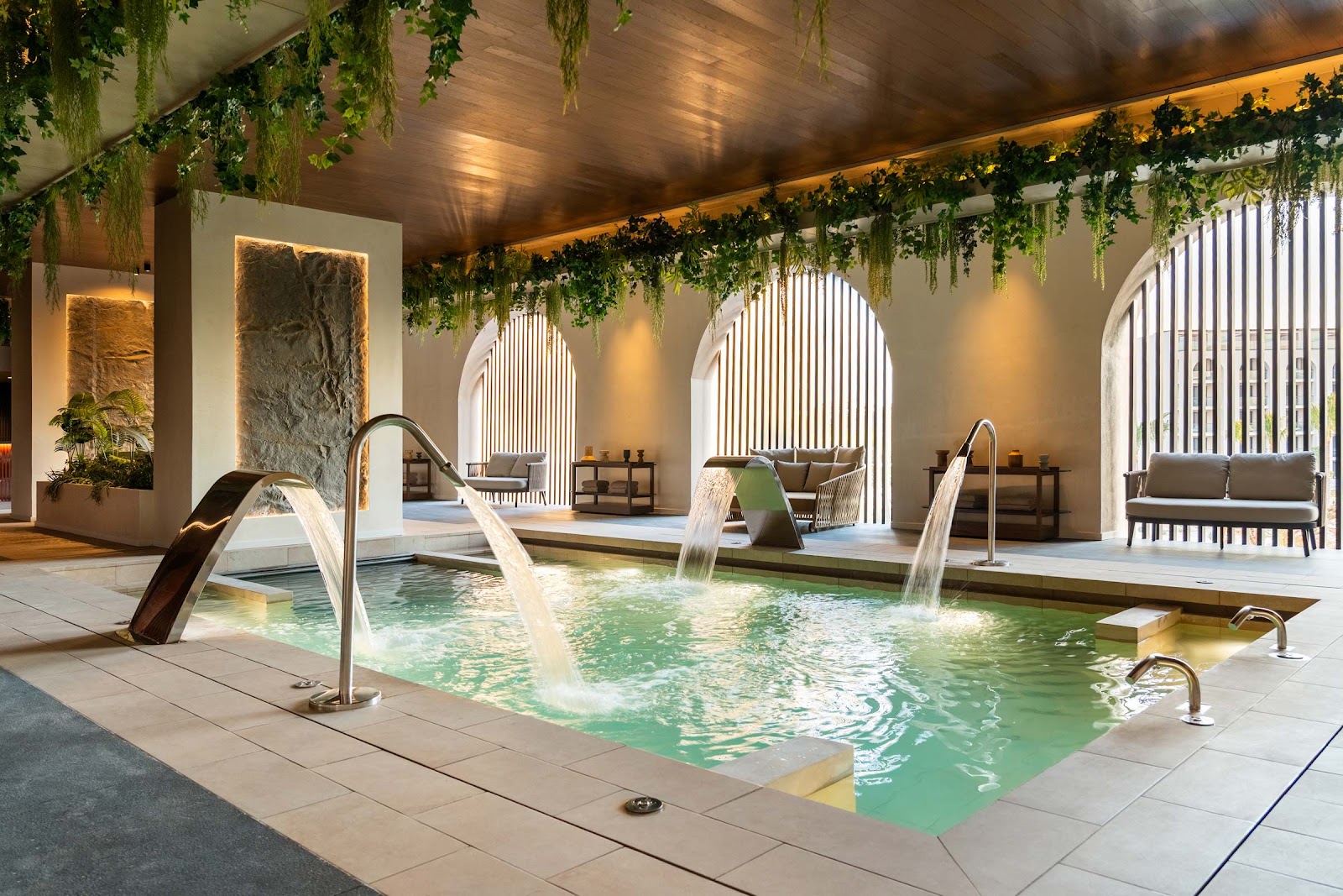 Indoor spa pool with water features, arched windows, hanging greenery, and lounge seating at Excellence Coral Playa Mujeres.