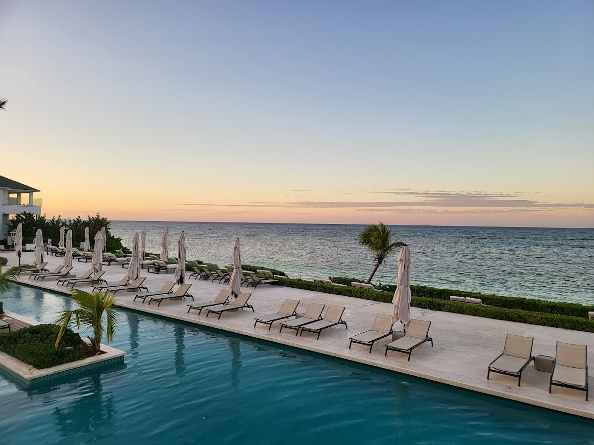 Resort pool and beach at sunset with lounge chairs, umbrellas, and ocean view at Excellence Oyster Bay.