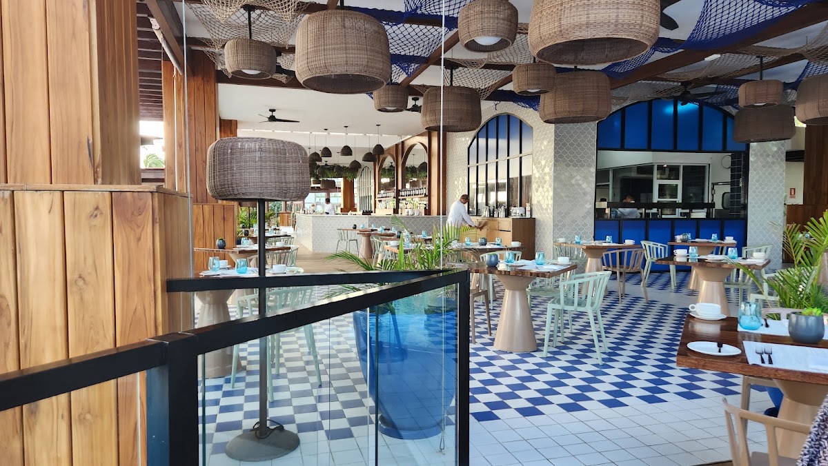 Open-concept dining area at Excellence Playa Mujeres with blue and white checkered floors, woven pendant lights, and a modern kitchen visible in the background.