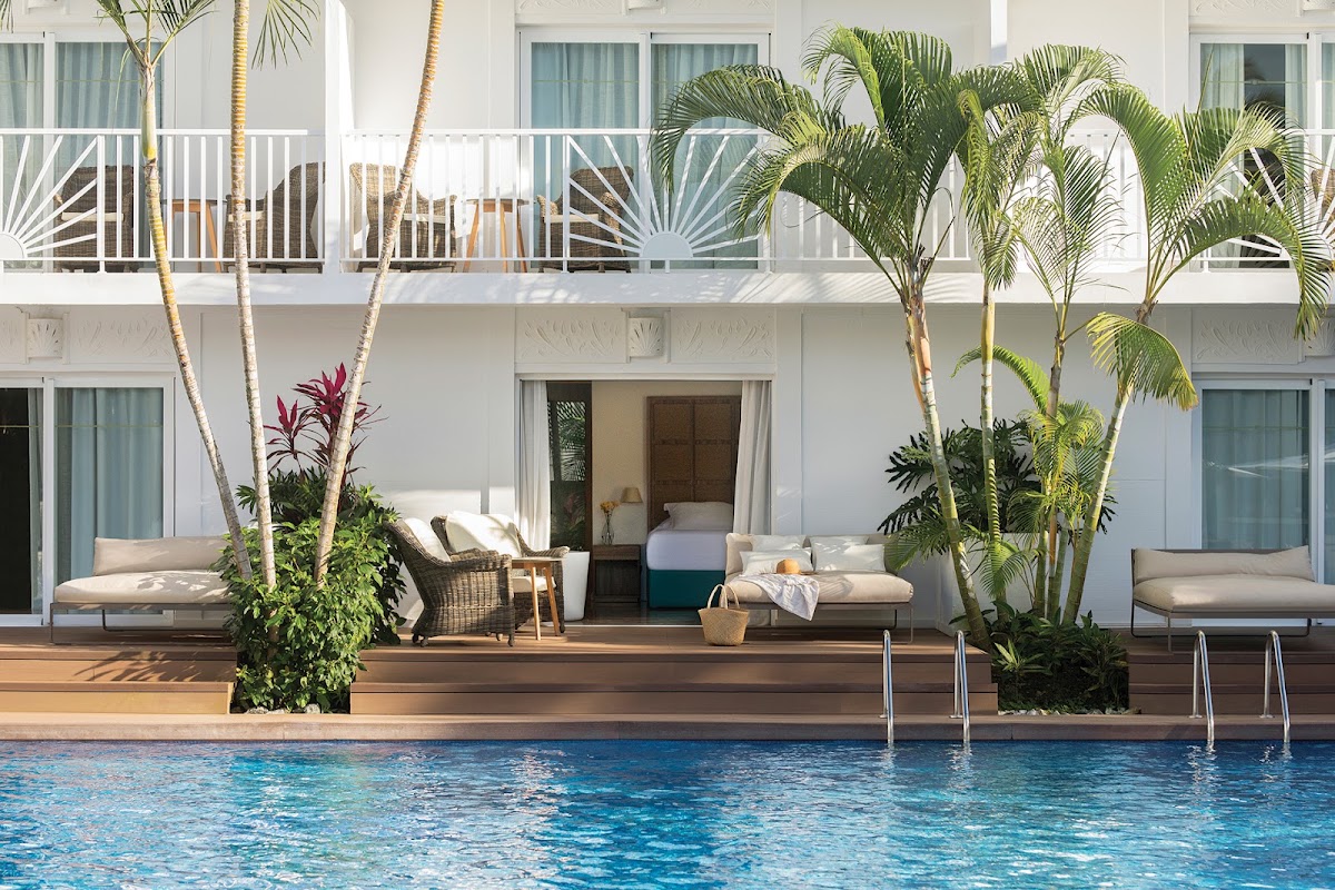 Pool deck with lounge chairs, potted palms, and white resort building with balconies at Excellence Punta Cana.
