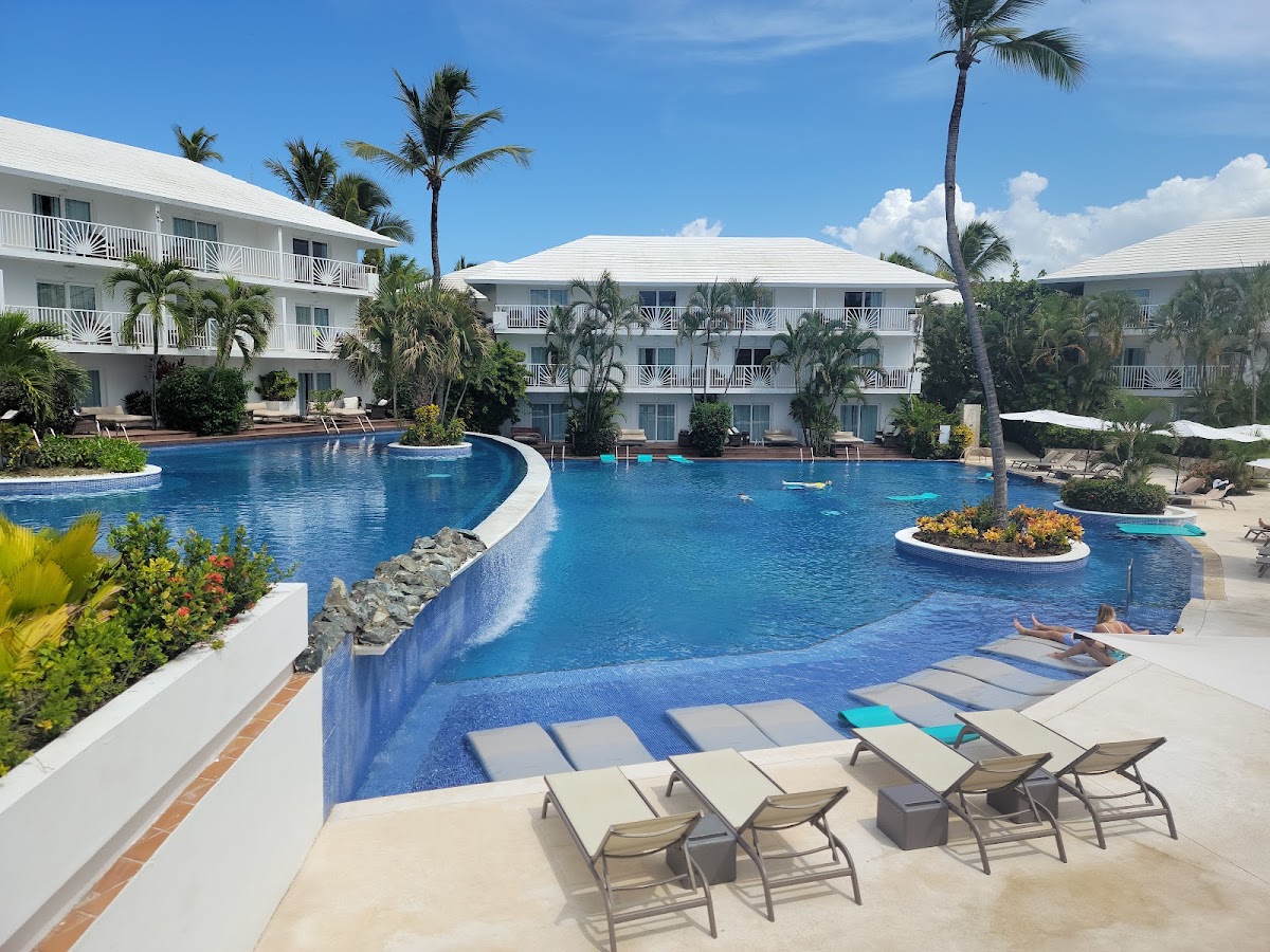Curved blue swimming pool surrounded by white buildings and palms at Excellence Punta Cana.