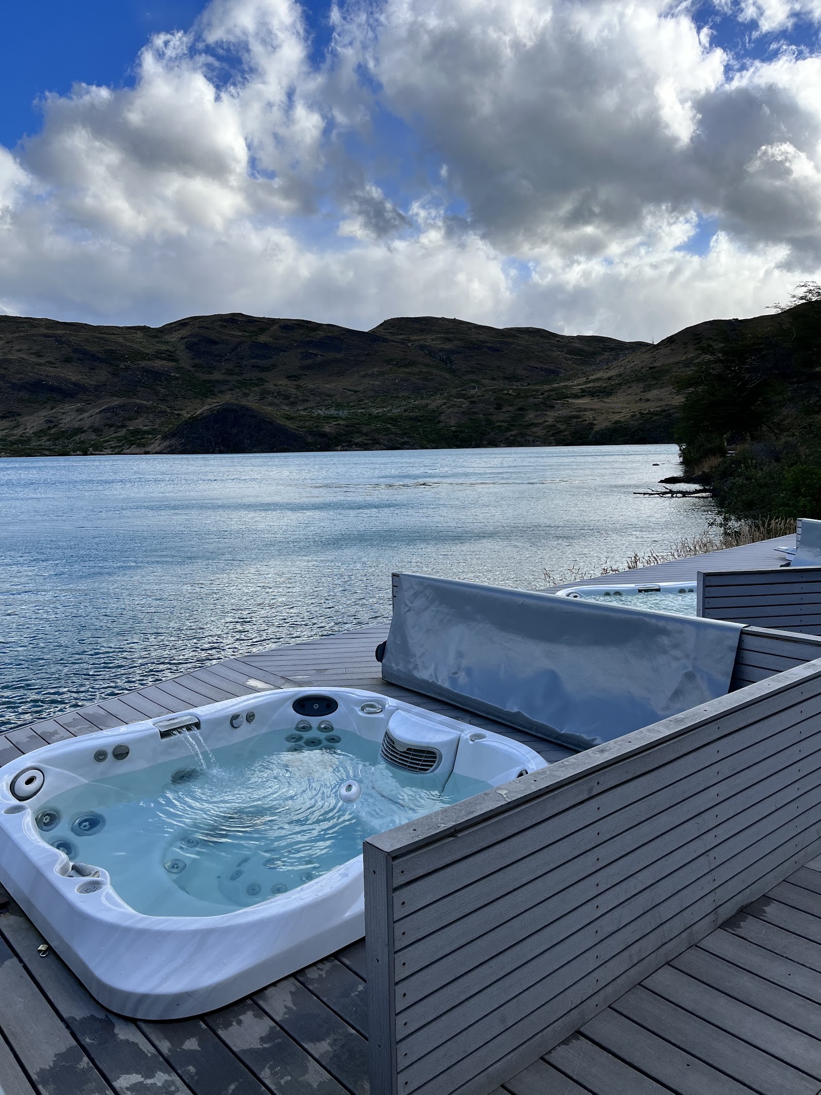 Hot tub on a wooden deck overlooking a calm lake with dark mountains and cloudy sky at Explora Torres del Paine.