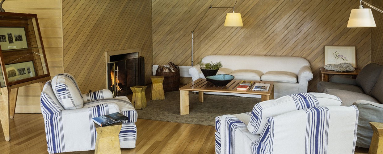 Lounge with striped armchairs, cream sofa, fireplace, and wooden furniture throughout the Explora Torres del Paine.