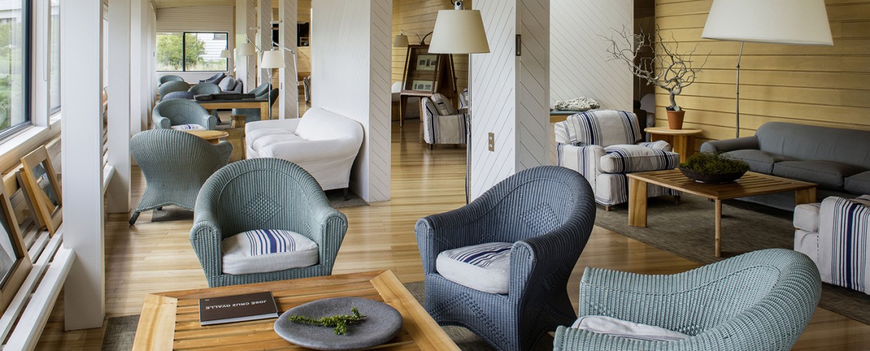 Modern lounge area with blue woven armchairs, wooden tables, and white pillars at Explora Torres del Paine.