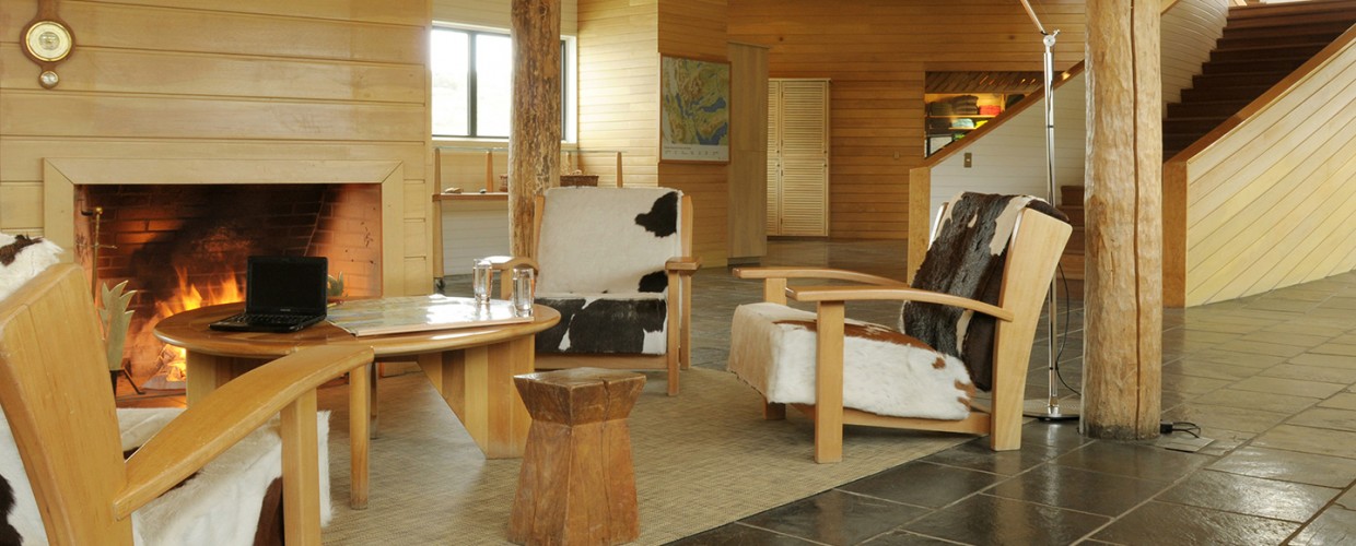 Wood-paneled lounge with fireplace, rustic furniture, and cowhide accents at Explora Torres del Paine.