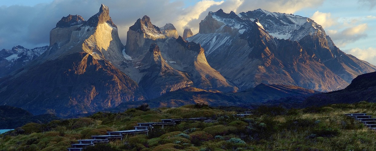 Blue lodge buildings nestled in grassland with dramatic granite peaks of Torres del Paine rising behind under morning light.