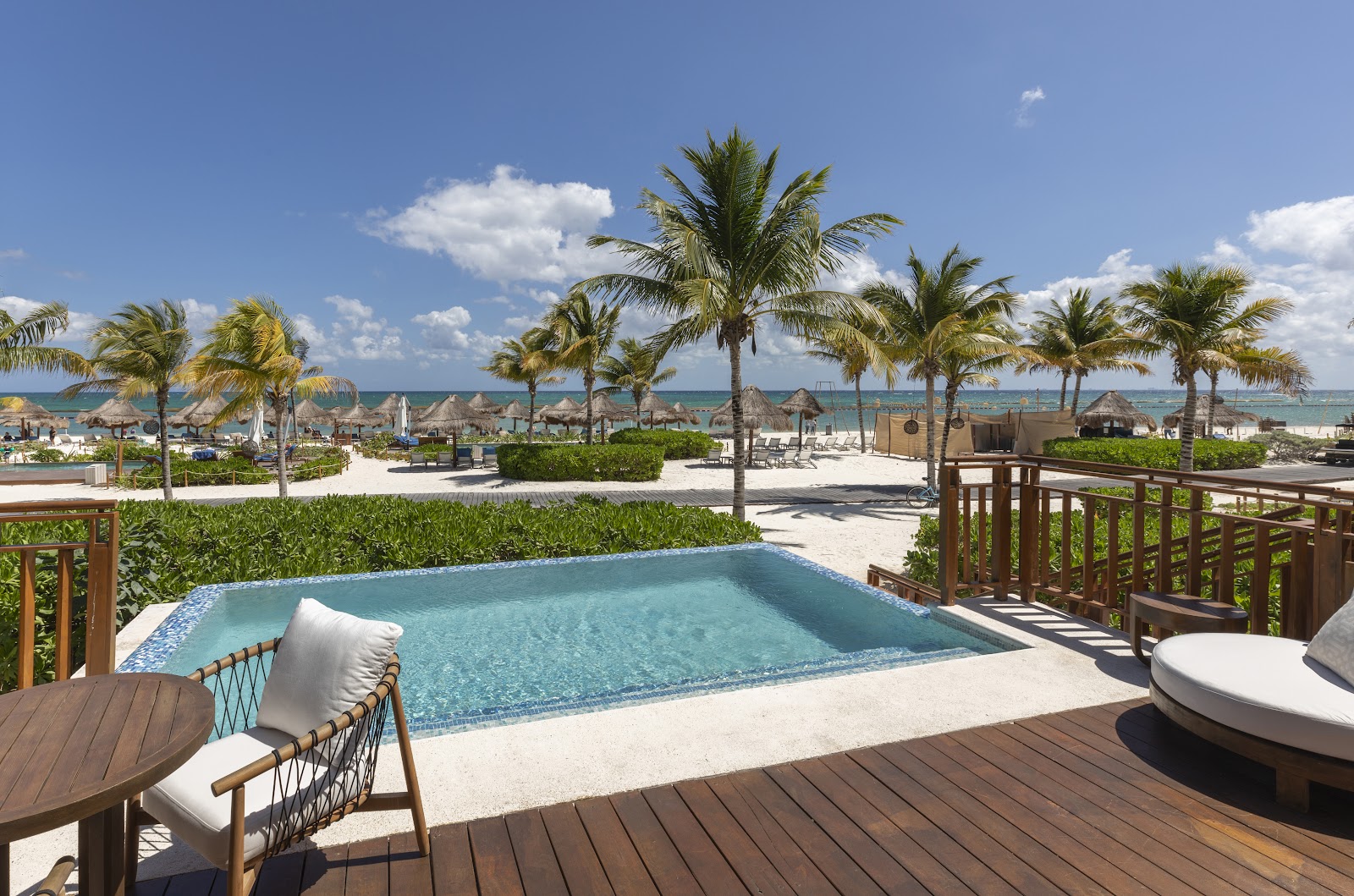 Private plunge pool on a wooden deck overlooking the beach, with palm trees and thatched palapas dotting the sand at Fairmont Mayakoba.