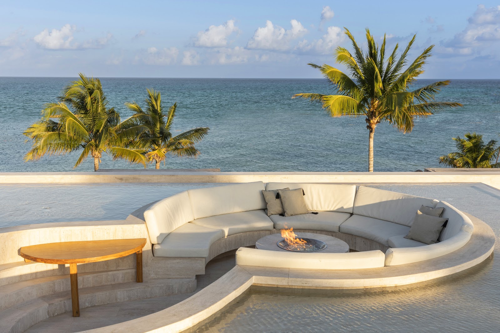 Wooden lounge chairs with blue cushions on a covered terrace overlooking a lagoon, mangrove forest, and distant buildings at Fairmont Mayakoba.