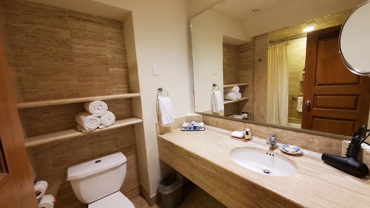 Fiesta Americana Puerto Vallarta bathroom with travertine countertop, large mirror, stacked towels on built-in shelves, and walk-in shower with yellow curtain.
