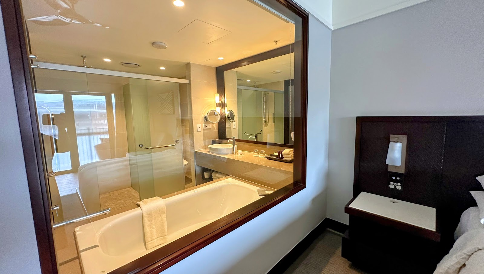 Resort bathroom with glass-enclosed shower, white soaking tub, and large mirror above dual vanity sink.